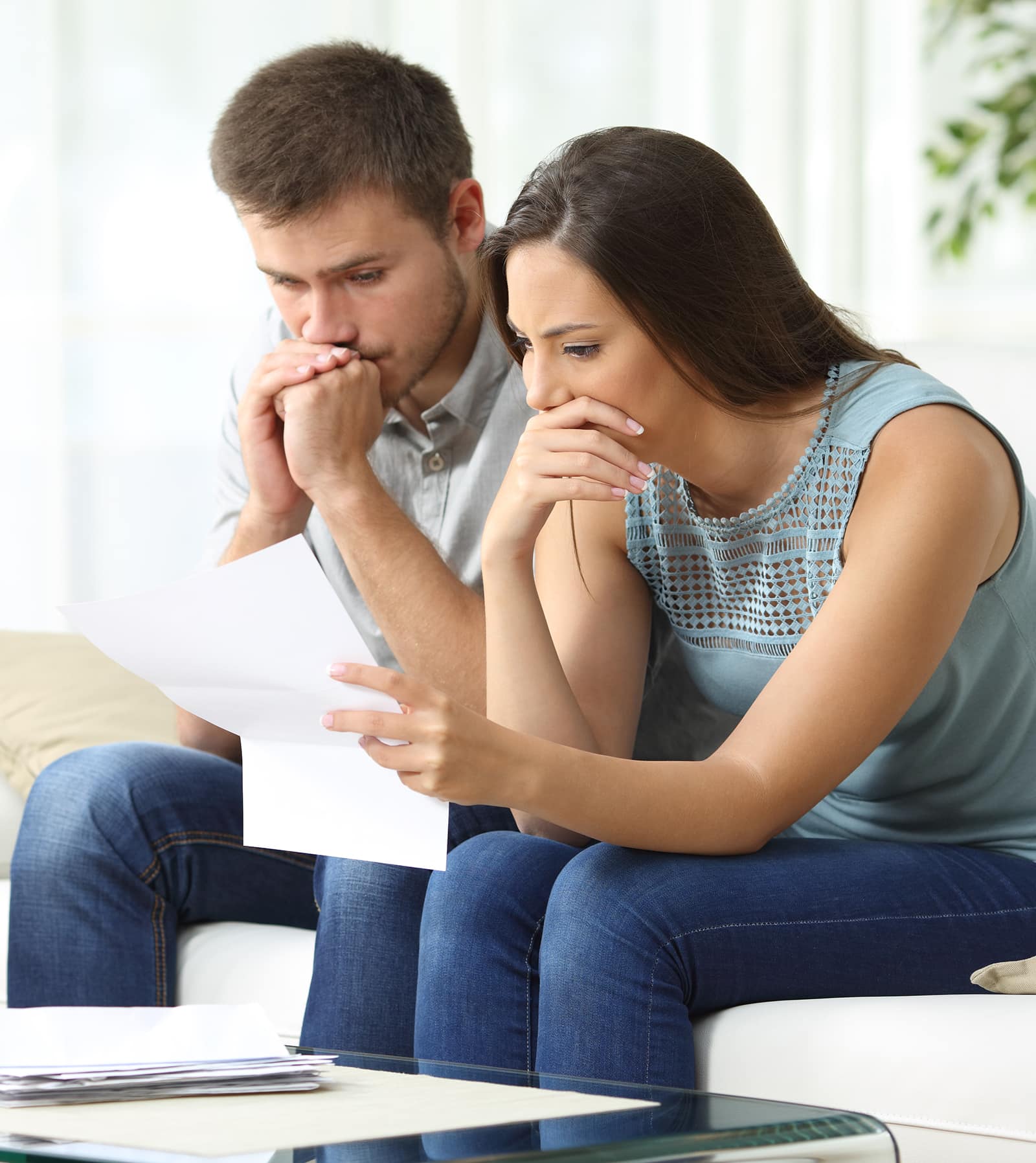 Foreclosure help in Oklahoma Worried couple reading an important notification in a letter sitting on a couch in the living room at home